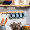 Detail shot of our peg rail being used under a plate rack. Blue cups hang from the rail. There is a kitchen utensil pot in the foreground. 