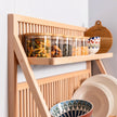 A side view of a plate shelf kitchen rack showing the detail of the wood. Food is being store in jars along the top shelf and a large bowl sits in the fore ground. Plates line the back. 