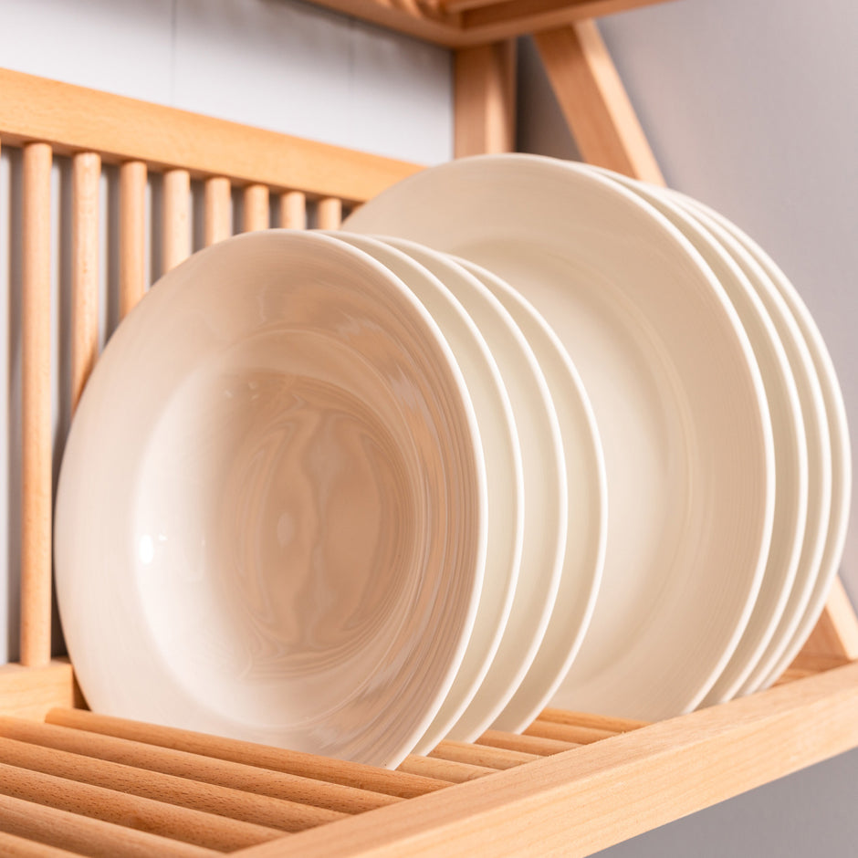 Detailed shot of plates being stored on the bottom shelf of our wall mounted plate rack. The wooden dowels hold the plates in place. In the foreground 
here are three ceramic bowls. 