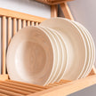 Detailed shot of plates being stored on the bottom shelf of our wall mounted plate rack. The wooden dowels hold the plates in place. In the foreground 
here are three ceramic bowls. 