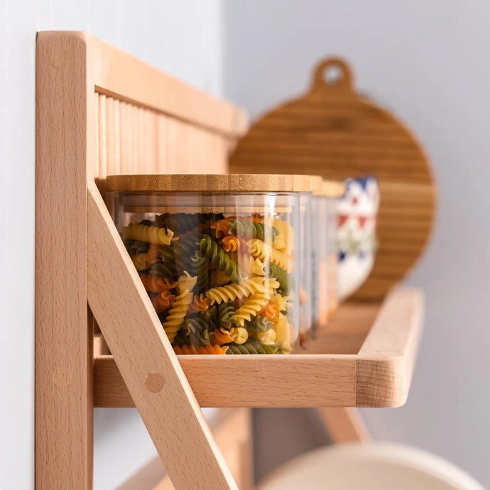 A close up view of the top shelf of our plate storage rack. Dried pasta is being stored in glass jars and there is a wooden chopping board in the back ground. 